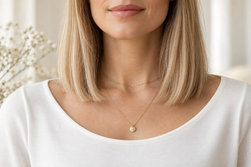 Schmuck zum Bob: kurze Goldkette über und längere Kette mit rundem Anhänger unter den Spitzen des Long Bobs
