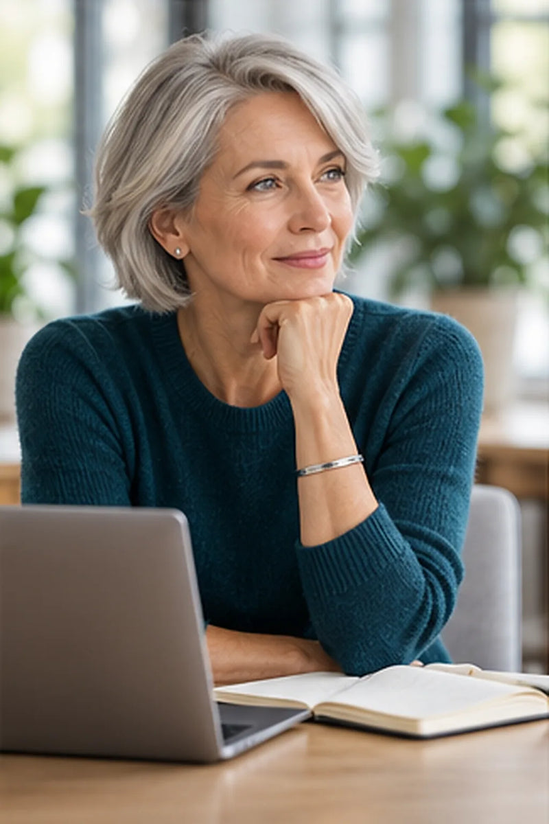 Business Casual ab 50: Frau im Kaschmirpullover in Petrol mit schlichtem Silberarmband am Konferenztisch